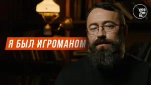 Man with a beard speaking in a cozy setting, illuminated by warm lighting, emphasizing a reflective moment.