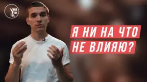 Young man in a white shirt gesturing while posing a thought-provoking question in Russian on a blurred background.