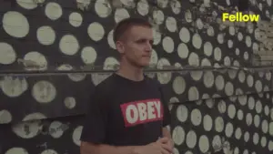 Young man in an "OBEY" t-shirt standing against a colorful polka dot mural, embodying urban street style.