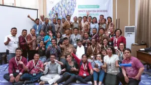 Group photo of diverse participants at a conference, posing together with cheerful expressions and raising hands in celebration.