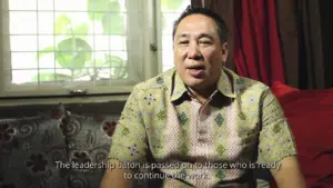 A man in a patterned shirt speaks about leadership and continuity, seated in a cozy indoor setting with natural light.