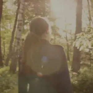 Person walking in a sunlit forest, surrounded by trees and greenery, creating a serene and peaceful atmosphere.