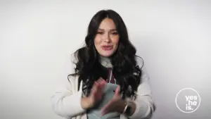 Young woman with long dark hair smiling and clapping against a plain white background, promoting positivity and engagement.