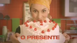 Woman in a headscarf holds a decorated cake with cherries, smiling joyfully in a vibrant kitchen setting.