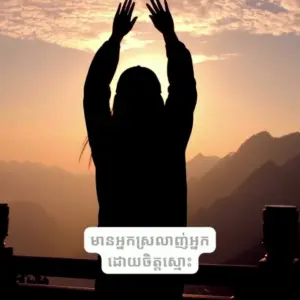 Silhouette of a person raising hands in celebration against a sunset backdrop in a mountainous landscape.