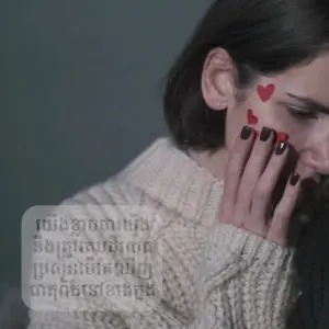 Woman in a cozy sweater with red heart designs on her face, expressing emotion against a muted backdrop.