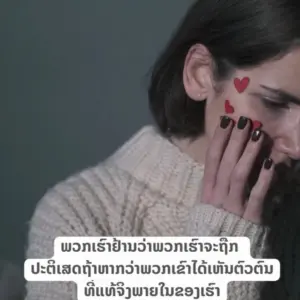 Woman with dark hair and painted nails, touching her face adorned with heart stickers, expressing emotion.