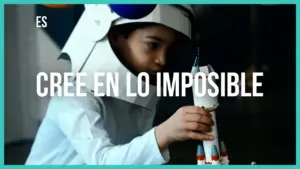 Child in a cardboard rocket hat assembling a model rocket, encouraging creativity and imagination with the phrase "Cree en lo imposible."