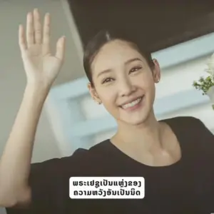 Smiling woman waving with a welcoming expression, showcasing friendly demeanor in a bright indoor setting.