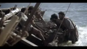 Men working on a wooden boat by the shore, showcasing teamwork and craftsmanship against a backdrop of water.