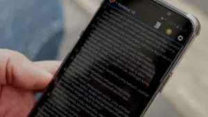 Close-up of a person's hand holding a smartphone displaying a text-heavy screen with a clear notification bar.