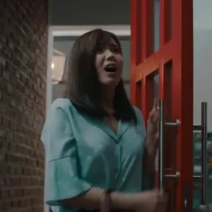 Woman in a light blue shirt excitedly opening a vibrant red door in a modern interior setting.