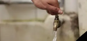 Person turning on a faucet with water flowing, highlighting plumbing and home maintenance.