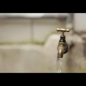 Brass faucet with water flowing freely, set against a blurred background showcasing a clean, refreshing environment.