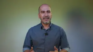 Middle-aged man in a gray shirt gesturing, with a blurred green background, conveying confidence and engagement.