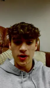 Portrait of a young man with curly hair wearing a grey hoodie, sitting comfortably on a couch.