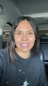 Smiling woman with long hair in a car, showcasing a casual look and friendly demeanor.