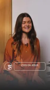 Smiling woman in an orange top, focusing on spiritual message in a cozy indoor setting.