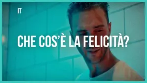 Man smiling in a bright, colorful setting with the phrase "Che cos’è la felicità?" prominently displayed.