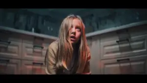 A frightened girl with messy hair sits on a kitchen floor, highlighting a dramatic and tense moment in the scene.