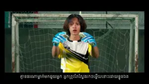 Goalkeeper in yellow and black uniform, wearing blue gloves, ready to defend the goal in an indoor soccer arena.