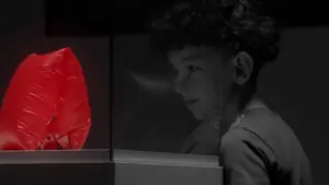 A child gazes curiously at a vibrant red sculpture, contrasting against a black and white background.