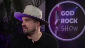 A man with a wide-brimmed hat sits next to a microphone sign for the God Rock Show, showcasing a vibrant event atmosphere.