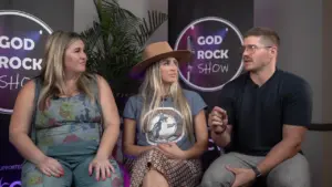 Three people discussing at the God Rock Show, featuring colorful backgrounds and stylish outfits in a lively setting.