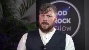 Man with a beard and casual attire speaking at a media event, featuring a backdrop with "Good Rock Show" branding.