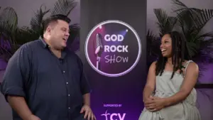 Two hosts smiling and engaging in conversation at the God Rock Show event with a vibrant backdrop.