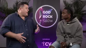 Two men engaged in conversation on the God Rock Show set, featuring a colorful backdrop and microphone elements.