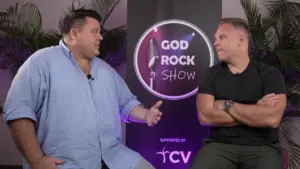 Two hosts discussing topics on the God Rock Show set, with vibrant branding and tropical decor in the background.