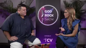 Host and guest engaging in discussion on the God Rock Show set, with vibrant backdrop and sponsor logo prominently displayed.