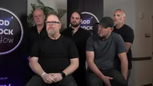 Five men in black shirts seated together, discussing topics on a set, with a backdrop promoting the "Good Rock Show."