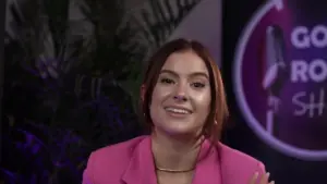 Smiling woman in a pink blazer, set against a colorful background with a microphone logo and lush greenery.