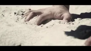 A close-up of a hand gripping sandy terrain, emphasizing strength and determination against a light background.