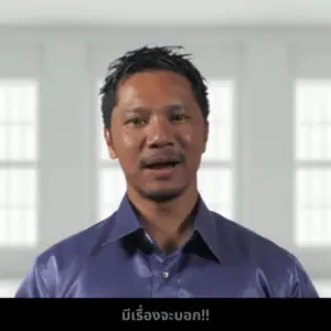 Man speaking in a purple shirt in a bright room, expressing enthusiasm, with text below in Thai.