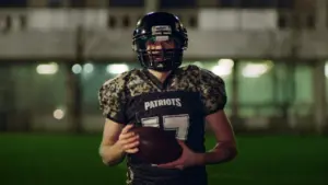 Football player in camouflage jersey holding a ball, standing on a field at night, showcasing athletic wear and team spirit.