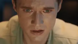 Close-up of a concerned young man with intense green eyes, focused on a screen, conveying deep emotion and tension.