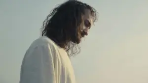 A serene man with long hair gazes downward against a calm sky, embodying peaceful contemplation and spirituality.