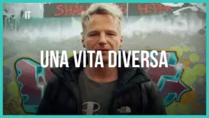 Man in a black jacket stands against a colorful graffiti wall, showcasing the phrase "Una Vita Diversa."