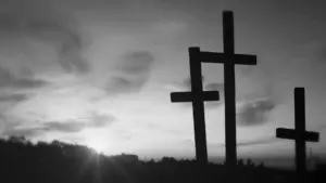 Silhouette of three crosses against a dramatic sunset sky in black and white, symbolizing faith and reflection.