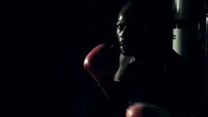 Dynamic close-up of a boxer in red gloves, silhouetted against a dark background, showcasing intense focus and determination.