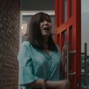 Woman in a blue shirt excitedly opens a bright red door in a modern, well-lit interior.