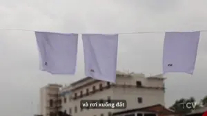 Three white shirts hang on a clothesline against a cloudy sky, with a building visible in the background.