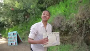 Person holding a newspaper in a lush outdoor setting, surrounded by greenery and natural light.