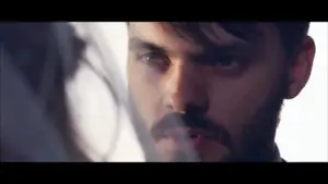 Intense close-up of a man's face, focusing on his piercing gaze and rugged features in a soft, blurred background.