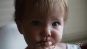 Close-up of a curious baby with blue eyes, gently sucking on fingers, conveying innocence and charm.