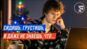 Young man in a checkered shirt looking thoughtfully at a laptop, with a Christmas tree in the background.