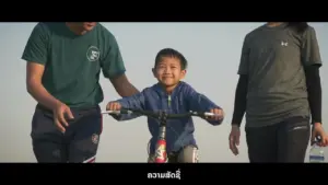 A smiling boy rides a bike, supported by two adults, enjoying a sunny day outdoors.